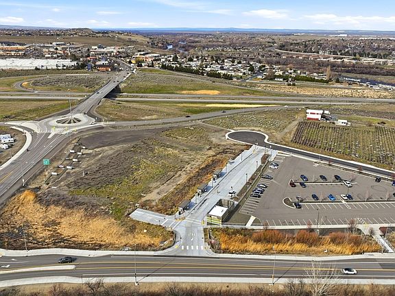 Wide aerial of the Queensgate corridor with the parcel boundary visible, the BFT transit station, the roundabout, and Richland's residential neighborhoods extending into the distance